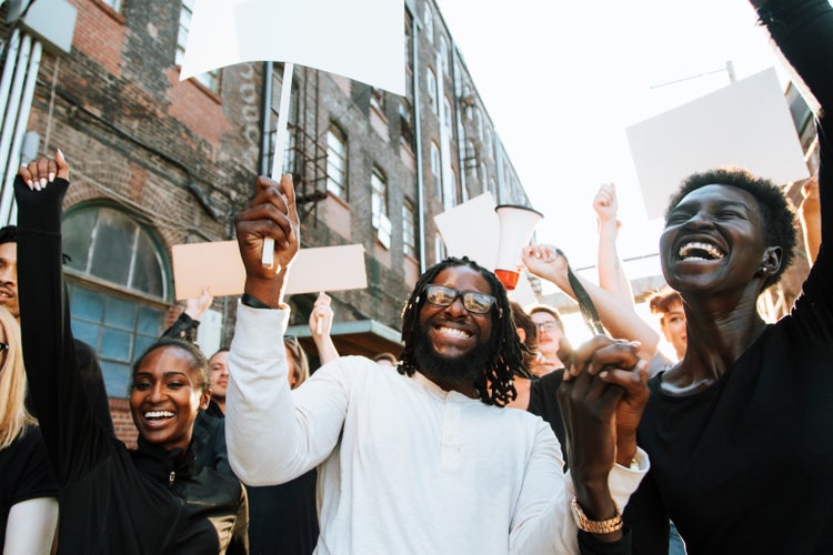 A group of smiling protesters marches down a street, holding blank signs and banners.