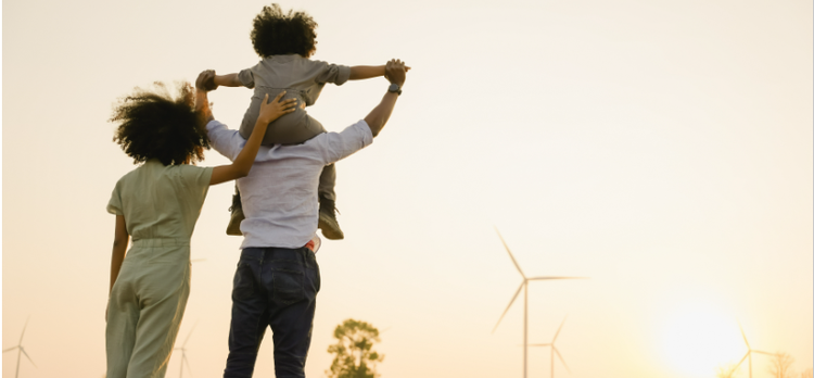 a family with their backs to the camera posing for a photo in a field with windmills