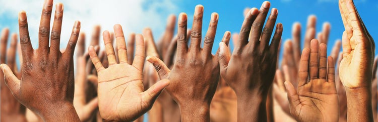 A group of many raised hands with diverse skin tones against a blue sky.