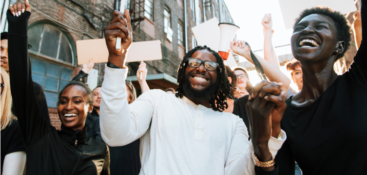 a smiling crowd protesting while holding signs and megaphones