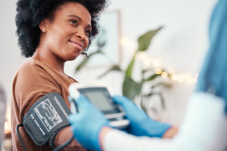 a woman smiling up at her nurse who is taking the woman's blood pressure