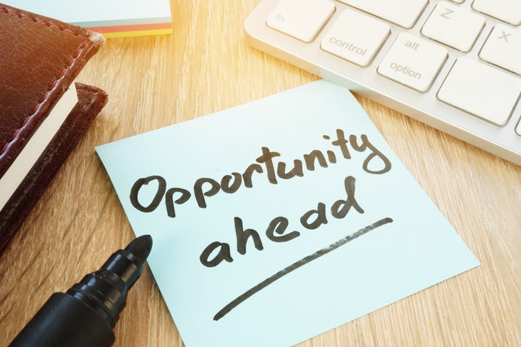 A blue sticky note on a wooden desk reads "Opportunity ahead" in handwritten black ink, next to a marker and keyboard.