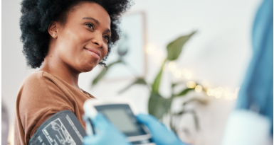 a woman smiling up at her nurse who is taking the woman's blood pressure