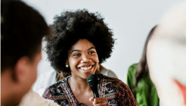 a woman smiling while speaking into a microphone